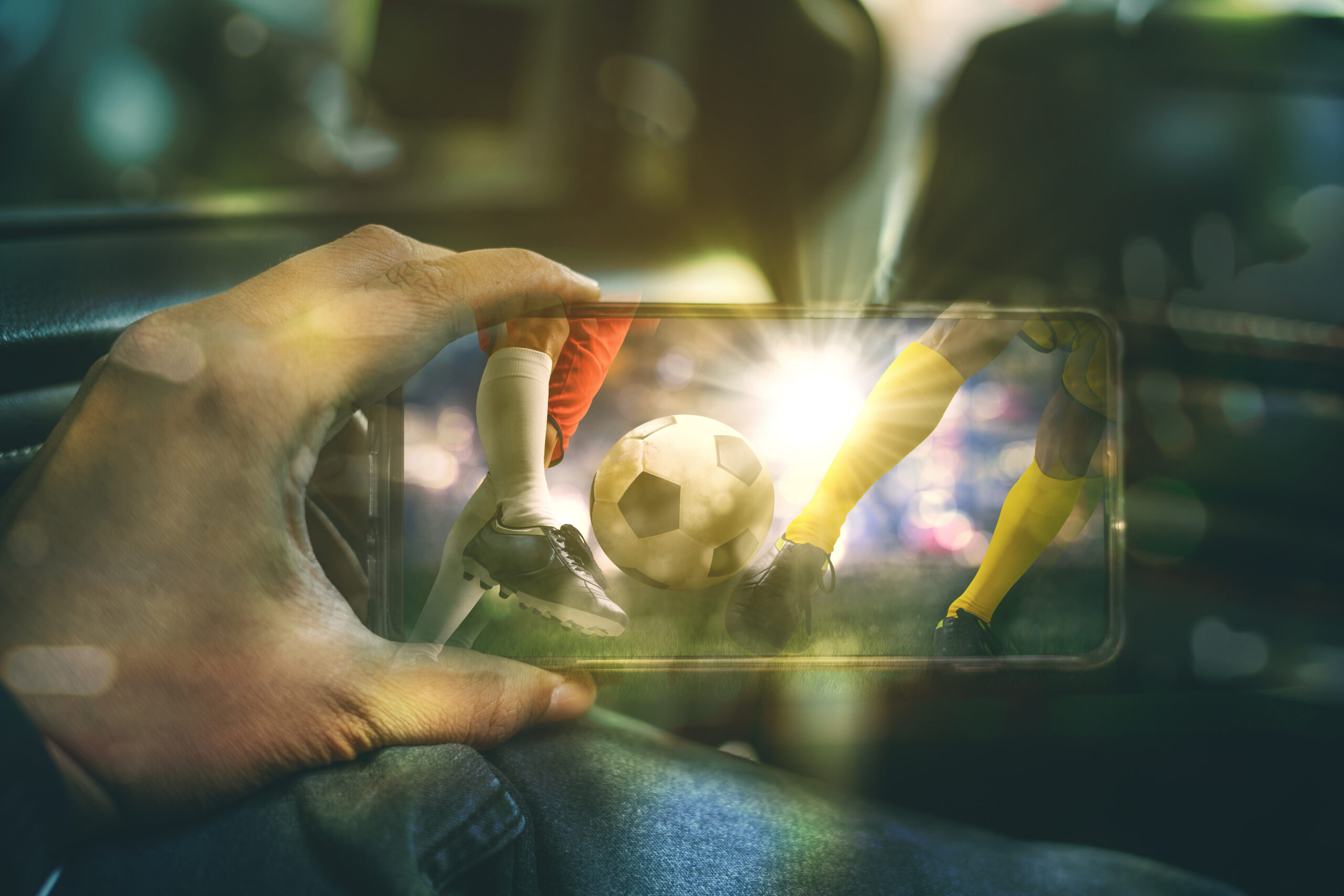 Uma mão branco segura um celular onde passa um jogo de futebol, representando as apostas esportivas online
